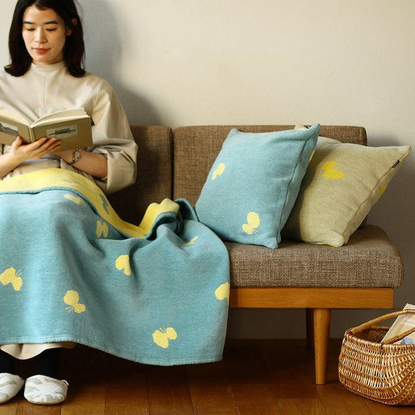 ソファに座って本を読む女性の横にシュニールコットン クッションカバー CHOUCHOを置いたシーン