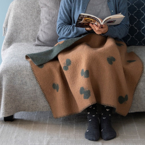 ウールブランケット CHOUCHO ミニサイズ グリーン/ベージュを裏返して膝に掛けた女性がソファに座って本を読むシーン